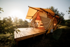 Cozy open glamping tent with light inside during sunset. Luxury camping tent for outdoor summer holiday and vacation. Lifestyle concept